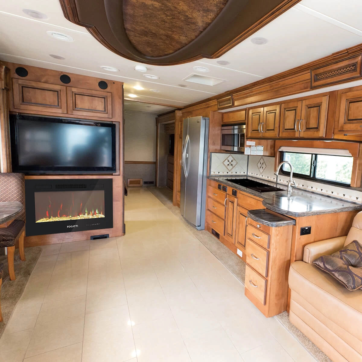 RV interior: Wooden cabinets, a FOGATTI cooktop in the kitchen area, and an FOGATTI electric fireplace in the living space, showing cozy travel living.