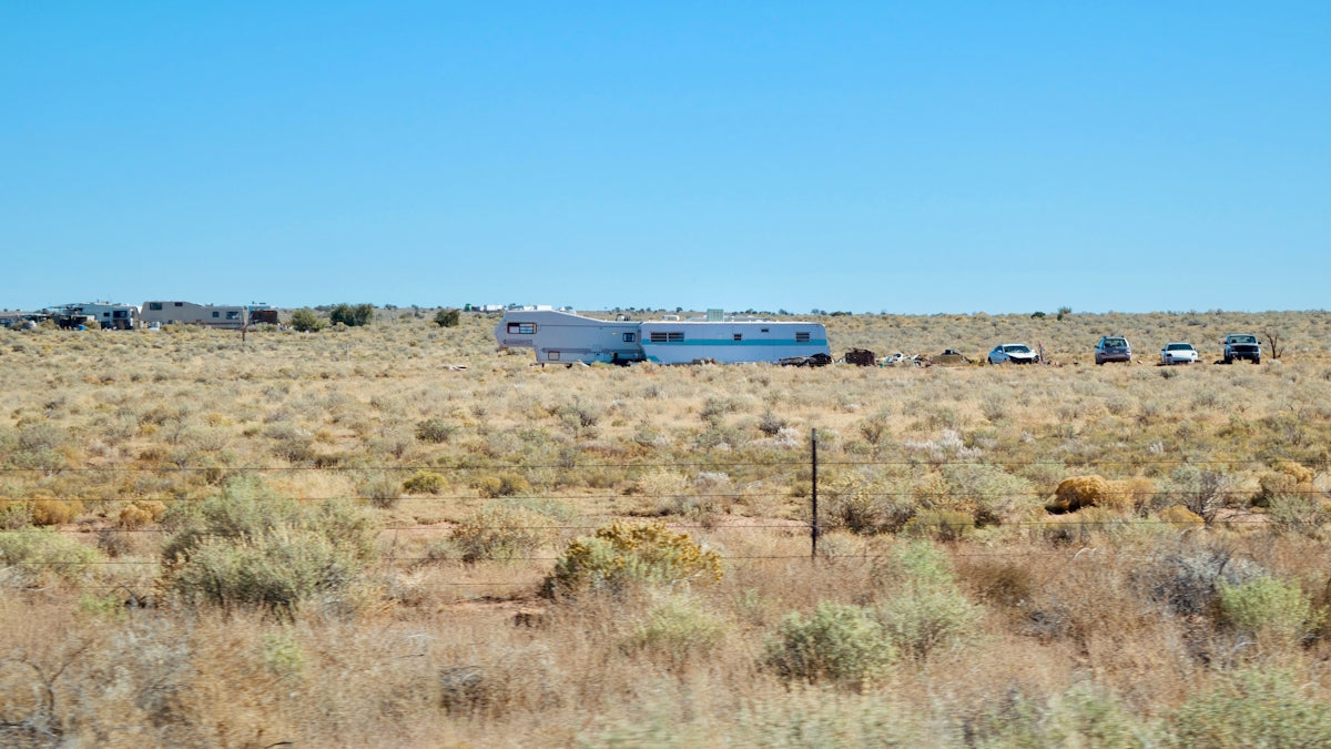 Rv and vehicles parked in a dry, brushy field.