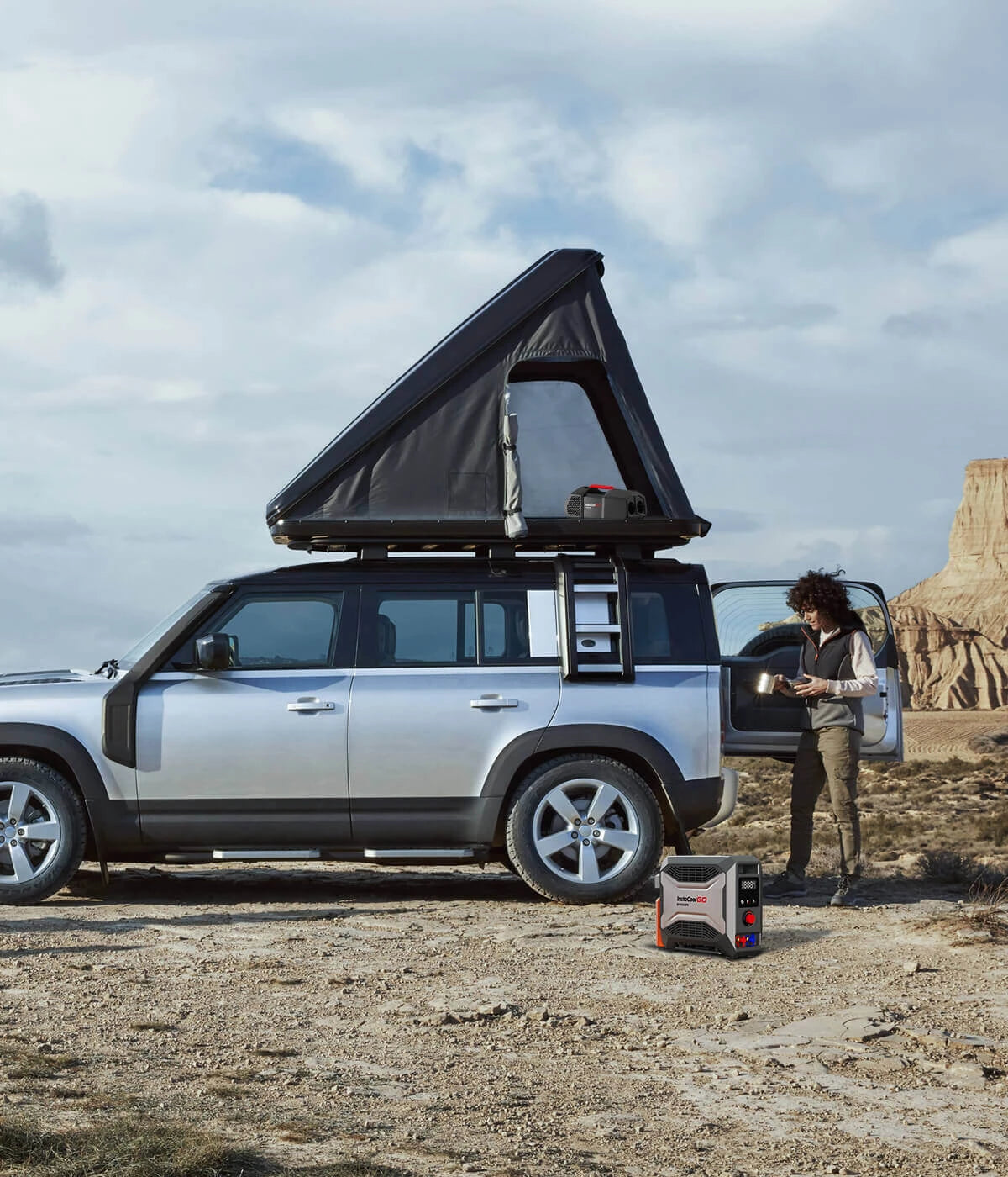 People camp in the wild with a silver SUV. The scene features the Fogatti InstaShower GO Outdoor Portable Water Heater, ready for outdoor use.