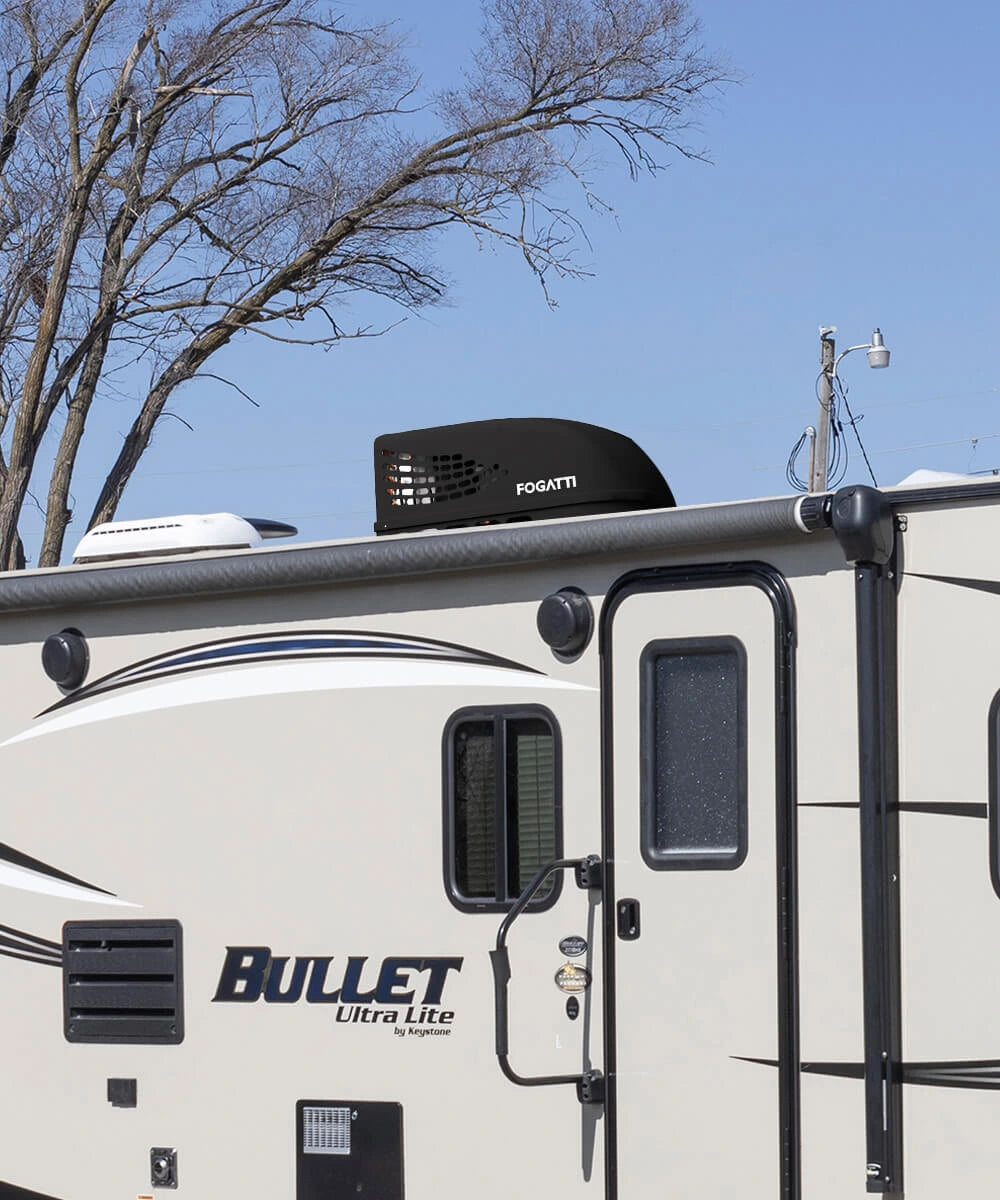 A black Fogatti InstaCool RV Rooftop Air Conditioner is installed on the roof of the RV, with trees and a clear blue sky in the background.