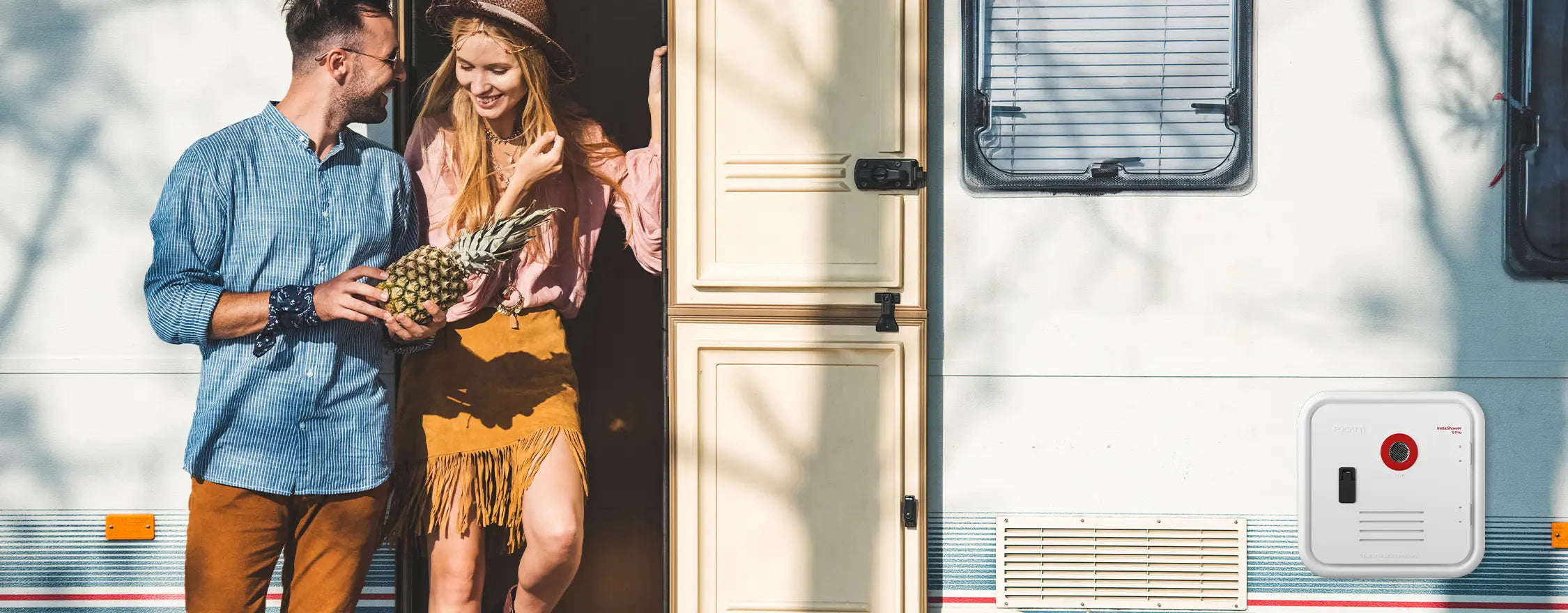 A couple stands at a caravan door, with a Fogatti water heater installed on the caravan body. 