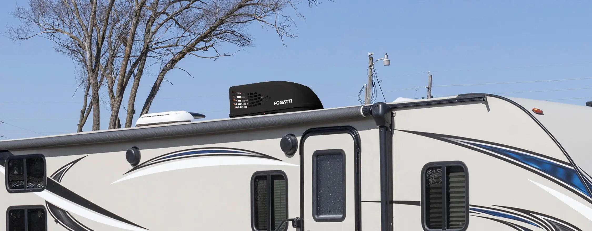 A black Fogatti InstaCool RV Rooftop Air Conditioner is installed on the roof of the RV, with trees and a clear blue sky in the background.